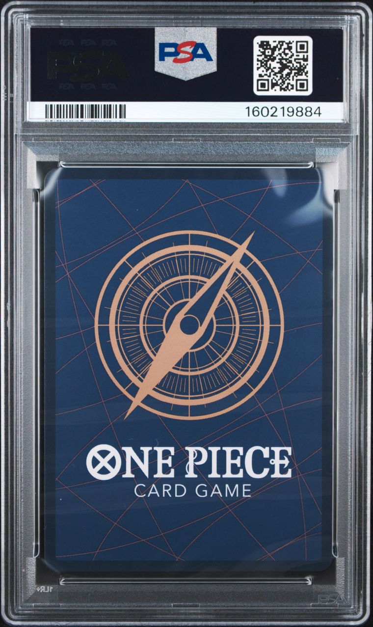 A PSA graded One Piece Card Game deck box inside a clear plastic grading case, showing a dark blue box with a gold compass design and white One Piece branding.